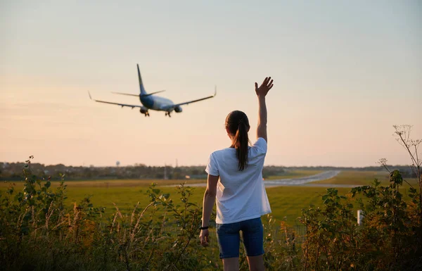 Vista trasera de mujer saludando mano a aterrizaje avión comercial — Foto de Stock