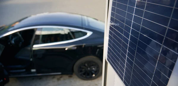Coche eléctrico negro estacionado cerca del panel solar. — Foto de Stock