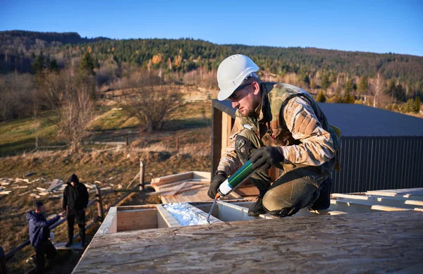 Male builder doing thermal insulation on roof of wooden frame house by polyurethane foam. — Foto Stock