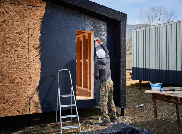 Boya silindiri kullanan erkek ressam, ahşap çerçeve inşa ederken dış boya işi yapıyor..