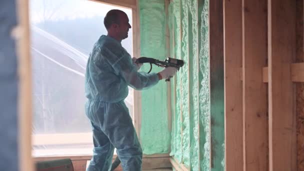Worker spraying polyurethane foam for insulating wooden frame house. — Stockvideo