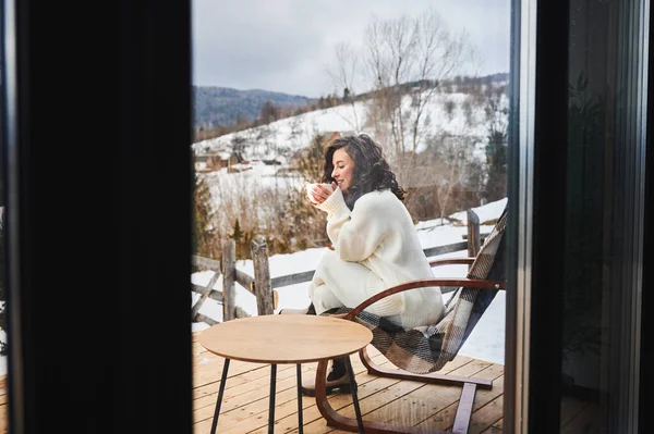 Woman enjoying winter holidays on terrace of contemporary barn house in the mountains. — Stockfoto