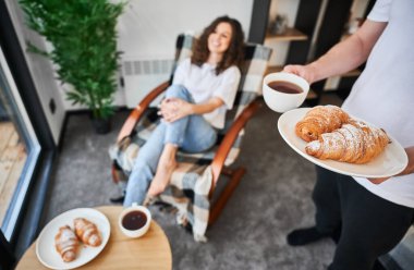 Man serving coffee and croissants to woman at home.