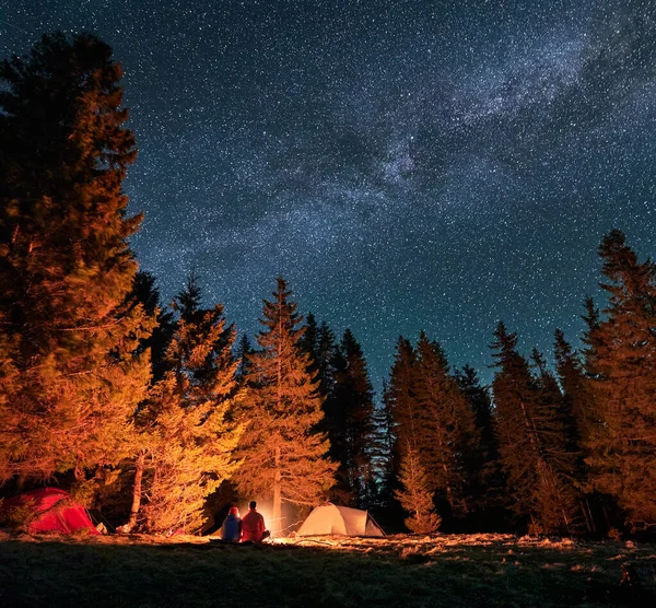 Erkek ve kadın açık havada yıldızlı bir gecede kamp alanında dinleniyorlar..
