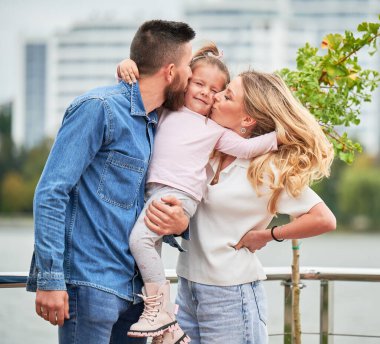 Mutlu bir anne ve baba sokakta kızını öpüyor..