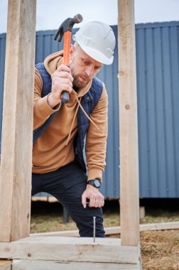 Yığınla temele ahşap çerçeve inşa eden bir işçi. Marangoz çekiçle tahta çivi çakıyor. Marangozluk kavramı.