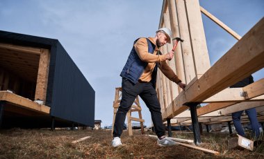 Yığınla temele ahşap çerçeve inşa eden bir işçi. Marangoz çekiçle tahta çivi çakıyor. Marangozluk kavramı.