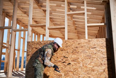 Marangoz, OSB panelinin duvarına çivi çakıyor. Ahşap çerçeve inşa eden bir işçi. Marangozluk ve inşaat konsepti.
