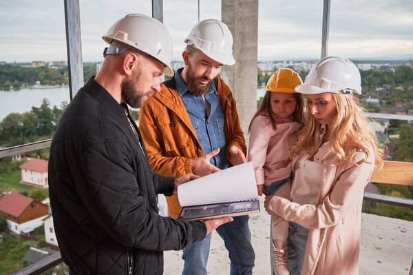Man and woman looking at catalogue while choosing interior design for new apartment with building worker. Couple with child planning home construction and redesigning with specialist.