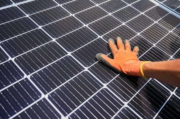 Close up of man solar technician installing solar modules for generating electricity through photovoltaic effect. Male hands in work gloves assembling photovoltaic solar panels.