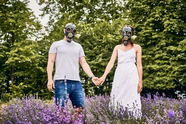 这对年轻夫妇戴着防毒面具 手牵手站在薰衣草地里的画像 过敏的人和盛开的薰衣草花 季节性过敏的概念 — 图库照片