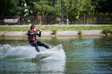 Wakeboardcu gölde sörf yapıyor. Genç sörfçü kablo parkında sörf yaparken eğleniyor. Su sporu, açık hava aktivitesi konsepti.