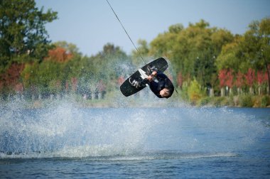 Wakeboardcu gölde wakeboard yaparken numaralar yapıyor. Genç sörfçü kablo parkında uyanırken eğleniyor. Su sporu, açık hava aktivitesi konsepti.