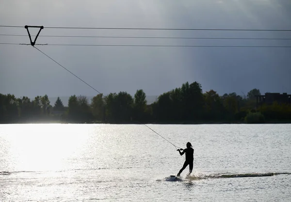 湖でウェイクボーダーサーフィンのシルエット ケーブルパークでウォーキングを楽しんでいるアスレチックマンサーファー ウォータースポーツ アウトドアアクティビティのコンセプト — ストック写真