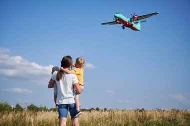 Genç bir annenin kucağında iki çocukla gökyüzünde uçan ticari uçaklara baktığı görüntüler. Yaşam tarzı ve seyahat konsepti.