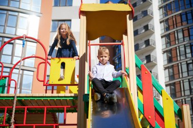 Neşeli erkek ve kız kardeşler oyun alanında eğleniyorlar. Genç bir oğlan ve kız şehir binalarının modern avlusunda oynuyorlar..