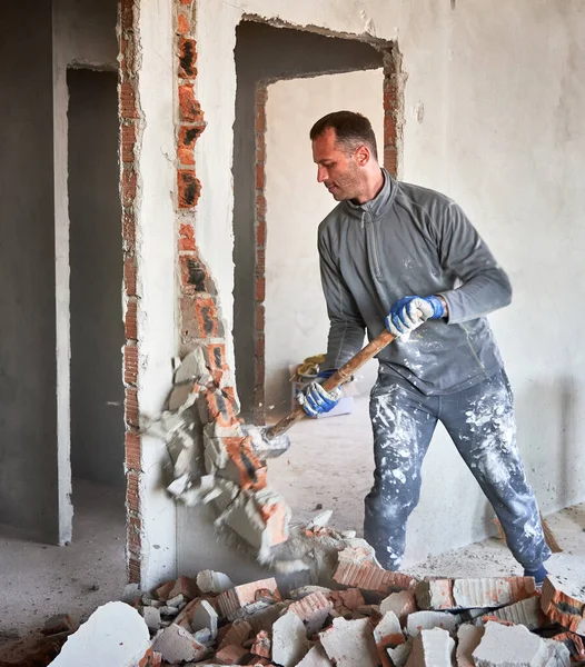 İki oda arasındaki duvarı yıkarken balyoz kullanan bir adam. Erkek işçi çekiç tutuyor ve tadilat altındaki apartmanın duvarlarını yıkıyor. Yıkım işleri ve ev yenileme konsepti.