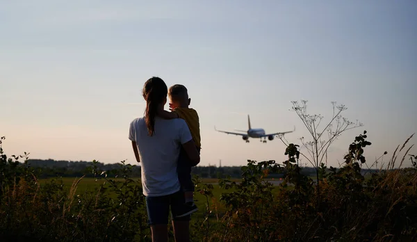 Silhouette of woman with child and looking to landing commercial airplane at the airport. Lifestyle and travel concept.