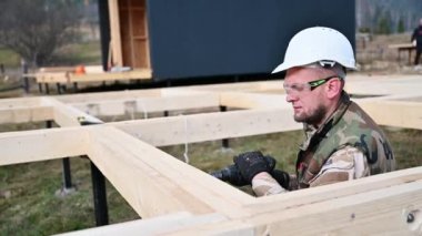 Ahşap çerçeve inşa eden adam. Gelecekteki kulübelerin ahşap çerçevesinde elektrikli matkapla delik açan işçiler. Marangozluk kavramı.