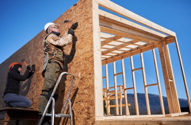 Marangozlar, OSB panelinin duvarına çivi çakıyor. İskandinav tarzı barnhouse 'da ahşap çerçeve inşa eden erkek işçiler. Marangozluk ve inşaat konsepti.