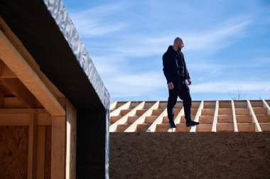 Erkek mimar ahşap çerçeve inşa ediyor. İnşaat alanında duran kel adam, güneşli bir günde iş kalitesini denetliyor ve arka planda mavi gökyüzü var..