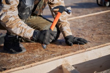 Marangoz, gelecekteki kulübenin çatısında OSB paneline çivi çakıyor. Ahşap çerçeve inşa eden işçilere yakın çekim. Marangozluk ve inşaat konsepti.