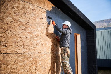 Boya silindiri kullanan erkek ressam, dış boyayı siyah renkte yapıyor. Ahşap çerçeve inşa eden bir işçi. Marangozluk ve inşaat konsepti.