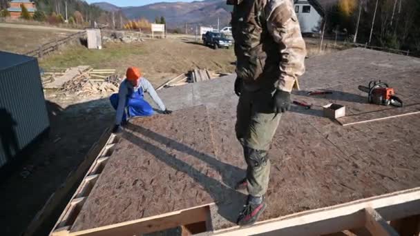 木匠在未来村舍的屋顶上安装木制Osb板 工人们正在建造木制框架结构房子 木工和建筑概念 — 图库视频影像