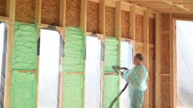 Erkek müteahhit ahşap iskeleti yalıtıyor. Adam işçi, gelecekteki kulübenin içine poliüretan köpük püskürtüyor, çoğul bileşen silah kullanıyor. İnşaat ve yalıtım konsepti.