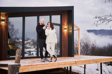 Mutlu kadın ve erkek kadeh tokuşturup kış günü dağlarda kutluyorlar. Birbirini seven bir çift, panoramik pencereli ahşap evin dışında alkollü içkinin keyfini çıkarıyor..