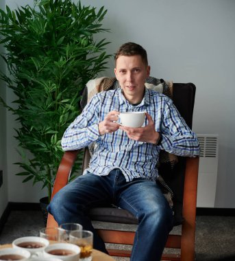 Çağdaş ahır evinde hafta sonları eğlenen genç bir adam. Sandalyede oturan erkek turistin portresi, elinde çayıyla yeni bir kulübede..