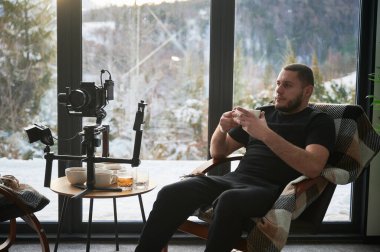 Kameraman koltukta dinleniyor, kamerasının yanında çay içiyor. Dengeleyici ekipmanına monte edilmiş..