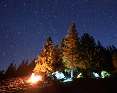 Geceleri yıldızlı gökyüzü ve şenlik ateşiyle turistik ekipmanlarla dolu kamp alanı, dağlarda dinlenmek ve dinlenmek için turist çadırlarıyla yürüyüş konsepti..