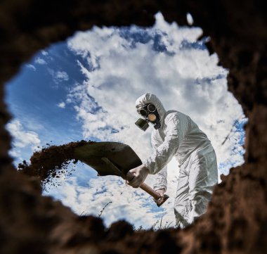 Gaz maskeli tanımlanamayan erkek bilim adamının tehlikeli bölgede toprak kazmak için kürek teçhizatı kullanması doğa ortamını analiz etmesi, kirliliği araştırması....