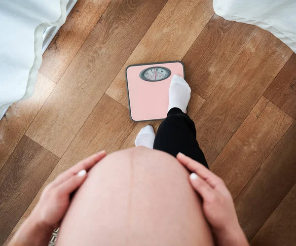 Unrecognizable pregnant woman with big tummy abdomen looking down while checking weight on electronic scales, cropped mother with belly worried about figure during maternity motherhood mood