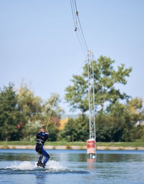 Gölde sörf yapan Wakeboard 'cuların arka görüntüsü. Genç sörfçü kablo parkında sörf yaparken eğleniyor. Su sporu, açık hava aktivitesi konsepti.