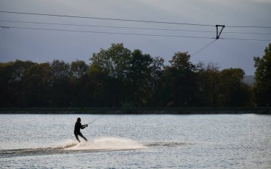 Gölde sörf yapan wakeboardcu silueti. Atletik sörfçü kablo parkında sörf yaparken eğleniyor. Su sporu, açık hava aktivitesi konsepti.