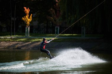 Wakeboardcu gölde sörf yapıyor. Genç sörfçü kablo parkında sörf yaparken eğleniyor. Su sporu, açık hava aktivitesi konsepti.