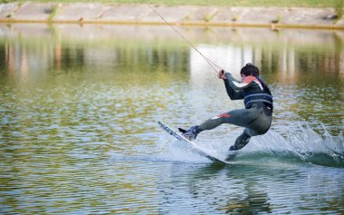 Wakeboardcu gölde sörf yapıyor. Genç sörfçü kablo parkında sörf yaparken eğleniyor. Su sporu, açık hava aktivitesi konsepti.