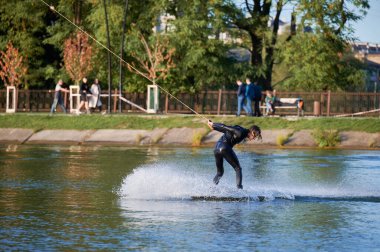 Wakeboardcu gölde wakeboard yaparken numaralar yapıyor. Genç sörfçü kablo parkında uyanırken eğleniyor. Su sporu, açık hava aktivitesi konsepti.