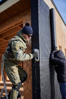 Erkek müteahhitler gelecekteki kulübelerin duvarına su geçirmez zar yerleştiriyorlar. Erkek işçiler ahşap çerçeve inşa ediyorlar. Marangozluk ve inşaat konsepti.