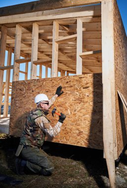 Marangoz, OSB panelinin duvarına çivi çakıyor. Ahşap çerçeve inşa eden bir işçi. Marangozluk ve inşaat konsepti.