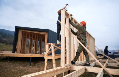 Yığınla temele ahşap çerçeve inşa eden bir işçi. Marangoz çekiçle tahta kirişe çivi çakıyor. Marangozluk kavramı.