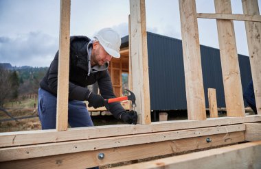 Man worker building wooden frame house. Carpenter hammering nail into wooden truss, using hammer. Carpentry concept.