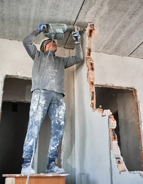 İşçi kıyafeti delme duvarında çekiç matkapla tam uzunlukta bir adam. Erkek işçi, tadilat altındaki dairedeki duvarı yıkarken matkap kullanıyor. Yıkım işleri ve ev yenileme konsepti.