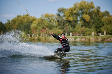 Wakeboardcu gölde sörf yapıyor. Genç sörfçü kablo parkında sörf yaparken eğleniyor. Su sporu, açık hava aktivitesi konsepti.