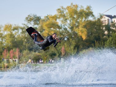 Wakeboardcu gölde wakeboard yaparken numaralar yapıyor. Genç sörfçü kablo parkında uyanırken eğleniyor. Su sporu, açık hava aktivitesi konsepti.