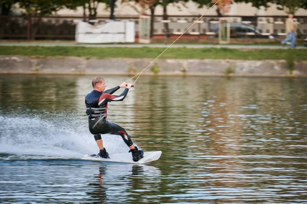 Wakeboardcu gölde sörf yapıyor. Genç sörfçü kablo parkında sörf yaparken eğleniyor. Su sporu, açık hava aktivitesi konsepti.
