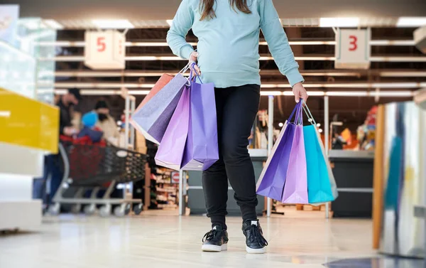 Unrecognizable female with belly holding paper bags feeling pain during shopping weekend for buy baby wear, cropped image of mom preparing to toddler have premature childbirth in store mall