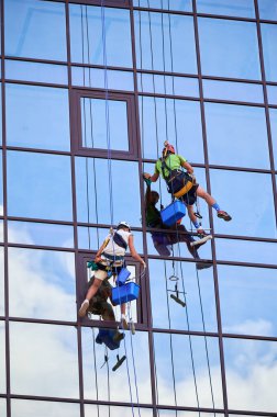 Endüstriyel dağcılık işçileri yüksek binaların camlarını yıkıyor, güvenli tırmanma halatlarına asılıyorlar. Gökdelenin dışında birlikte çalışan iki adam..